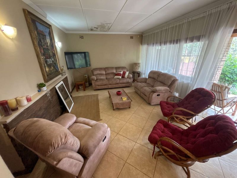 A spacious living room featuring tiled flooring, wall-mounted lighting, and large sliding glass doors leading to the exterior, with visible ceiling water damage.