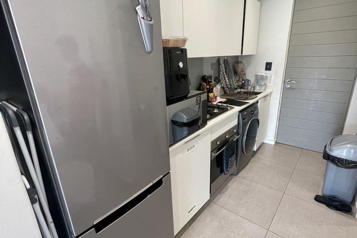Compact kitchen featuring modern white cabinetry, integrated oven, hob, and space for laundry appliances, finished with neutral floor tiling.