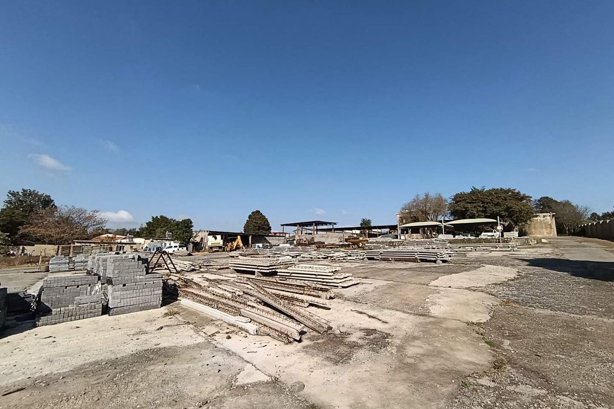 Expansive outdoor yard area on a small holding, featuring concrete paving and various industrial storage structures in the background.