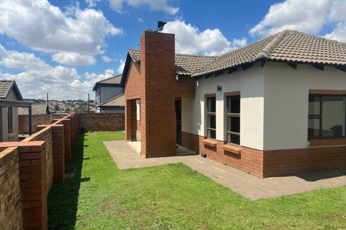 Rear view of the townhouse featuring a brick chimney, paved patio area, and a private garden enclosed by a brick boundary wall.