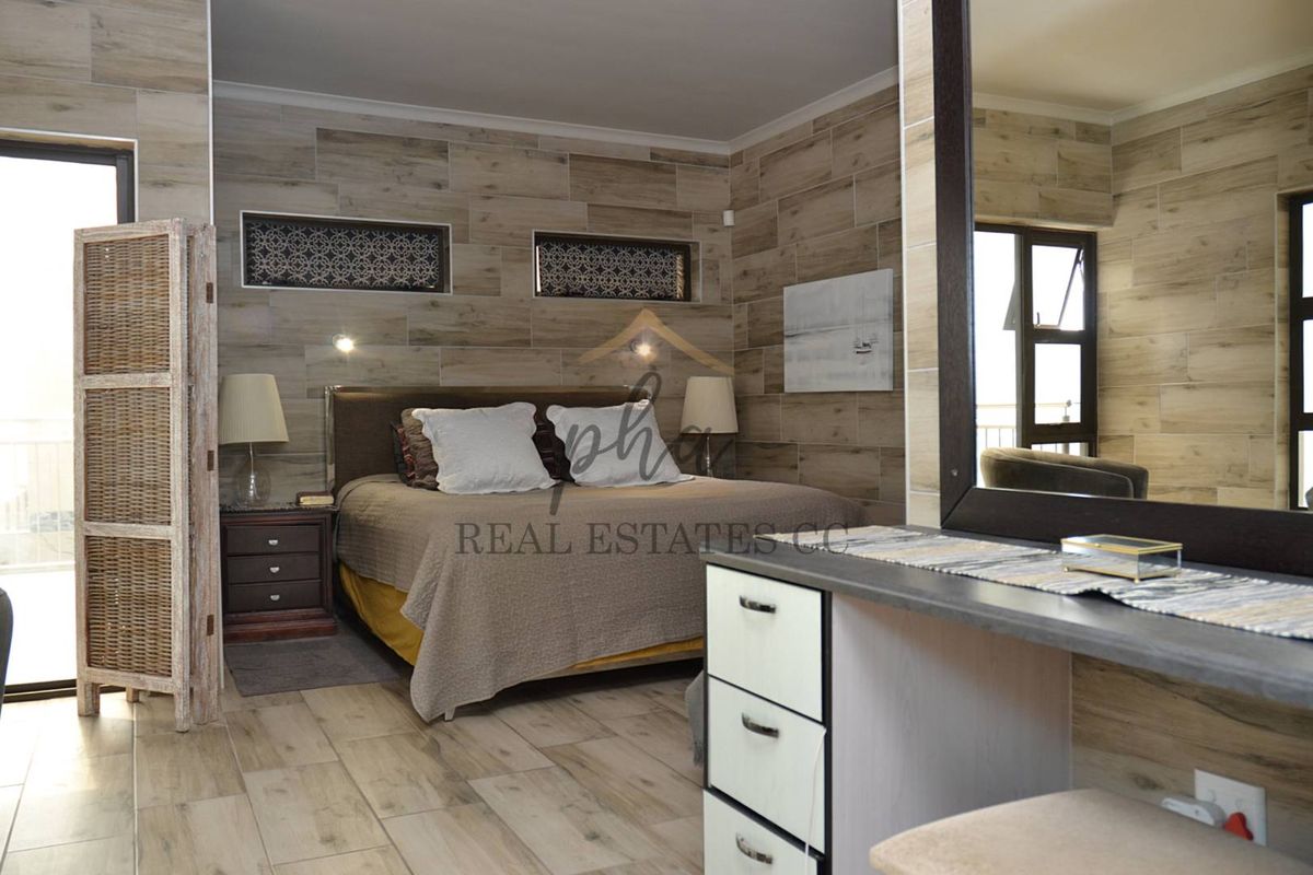 A well-appointed bedroom featuring wood-look tile wall cladding, built-in vanity unit, and large windows providing natural light.