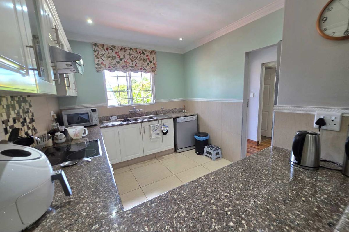 A functional kitchen featuring granite countertops, white cabinetry, a built-in hob, extractor fan, and tiled flooring with a window overlooking the exterior.