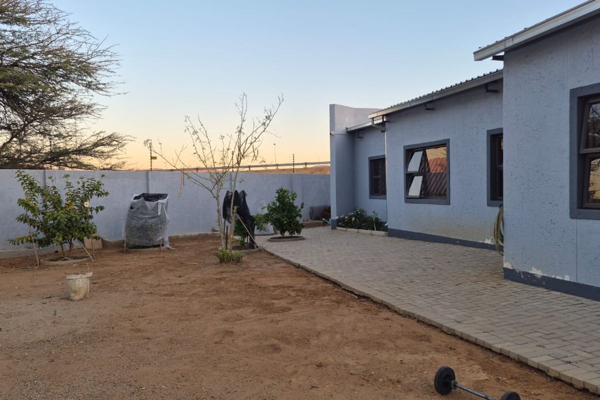 Rear exterior view of the house featuring a paved patio area, perimeter wall, and aluminium window frames.