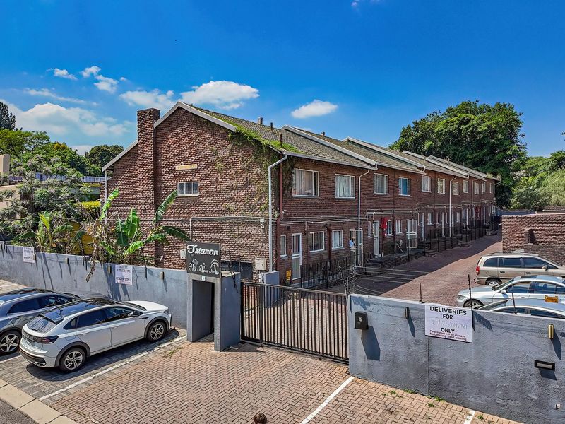 Exterior view of the Trianon apartment complex featuring a brick facade, secure gated entrance, and paved driveway parking area.