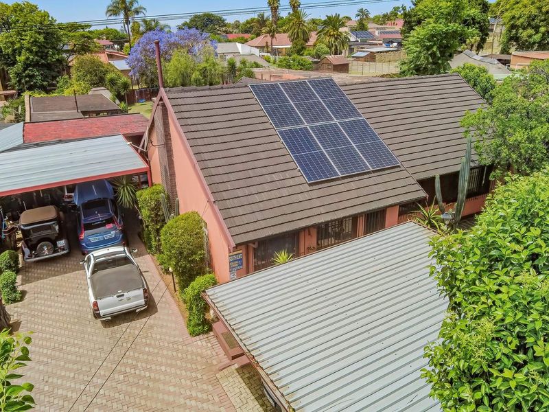 Aerial view of the property featuring a tiled roof with installed solar panels, a paved driveway, and a covered carport area.