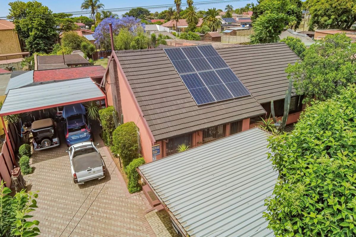 Aerial view of the property featuring a tiled roof with installed solar panels, a paved driveway, and a covered carport area.
