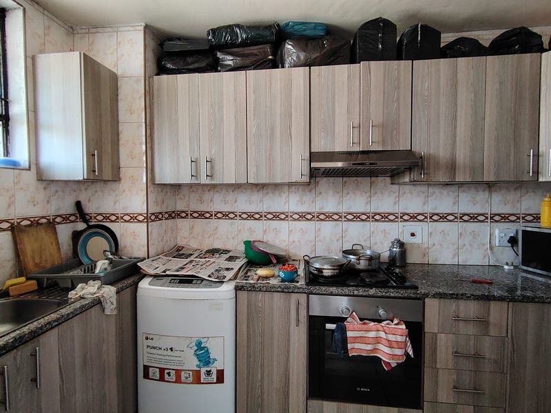 A functional kitchen featuring wood-look cabinetry, granite countertops, a built-in oven, and a gas hob with a stainless steel extractor fan.