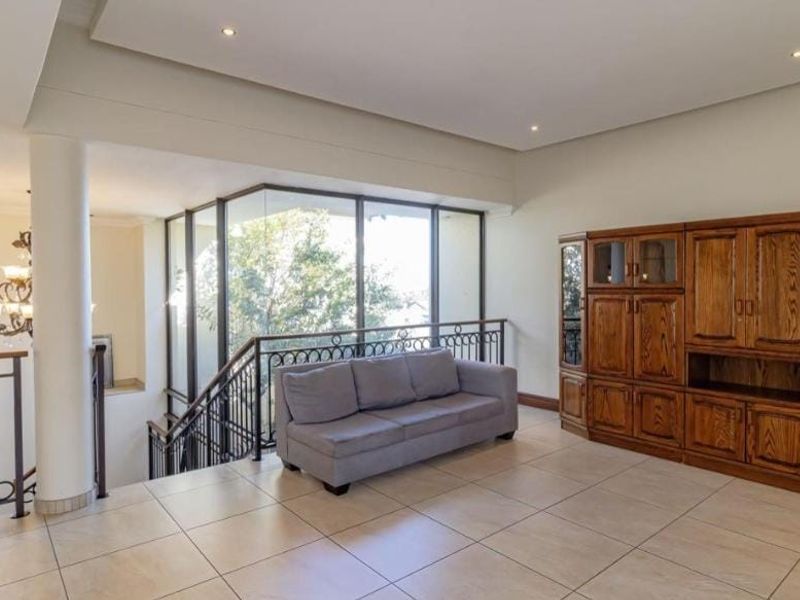 Spacious living area featuring tiled flooring, recessed lighting, and a wrought iron balustrade overlooking the staircase with large windows providing natural light.