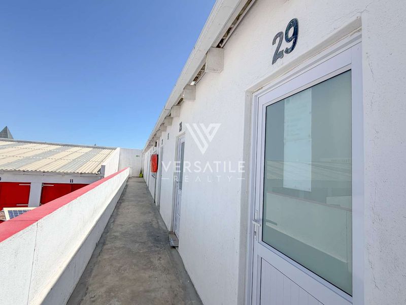 Exterior view of an industrial unit walkway featuring numbered access doors, concrete flooring, and a fire extinguisher mounted on the wall.