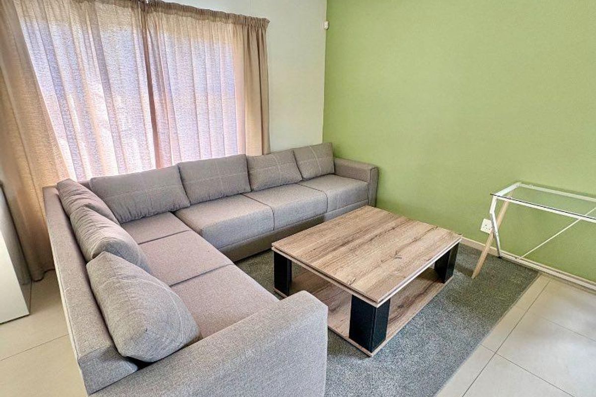 A living room featuring tiled flooring, a green accent wall, and large windows with curtain tracks.