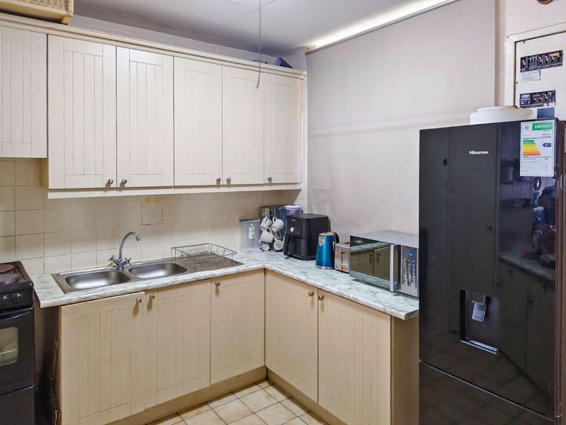 A functional kitchen featuring cream-colored cabinetry, a double bowl sink, laminate countertops, and tiled backsplash, offering a practical layout for daily use.