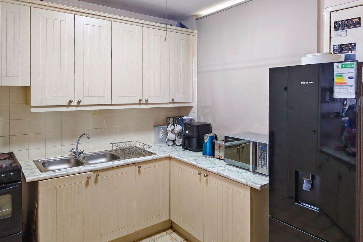 A functional kitchen featuring cream-colored cabinetry, a double bowl sink, laminate countertops, and tiled backsplash, offering a practical layout for daily use.