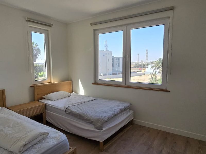 A bright bedroom featuring laminate flooring, built-in wardrobe storage, and large windows with roller blinds, offering a clean and functional living space.