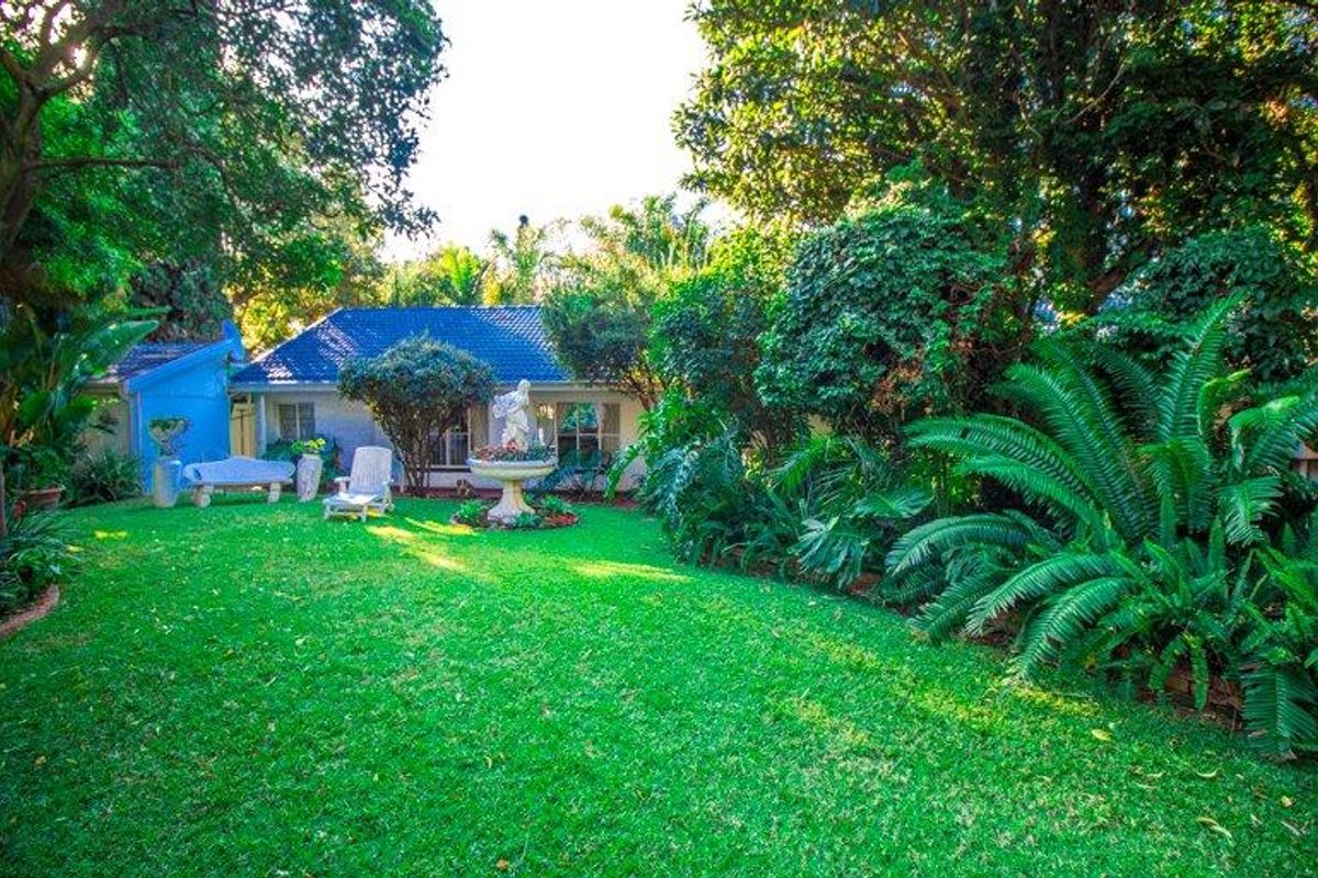 A lush, well-maintained rear garden featuring a manicured lawn, mature trees, and established shrubbery, providing a private outdoor setting for the home.