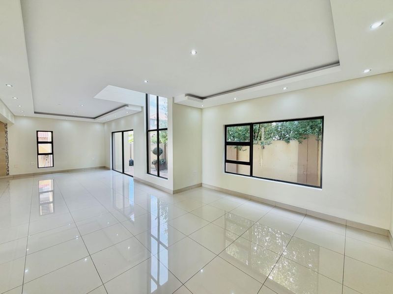 Spacious, open-plan living area featuring polished porcelain floor tiles, modern bulkhead ceilings with recessed lighting, and large aluminium-framed windows and sliding doors.