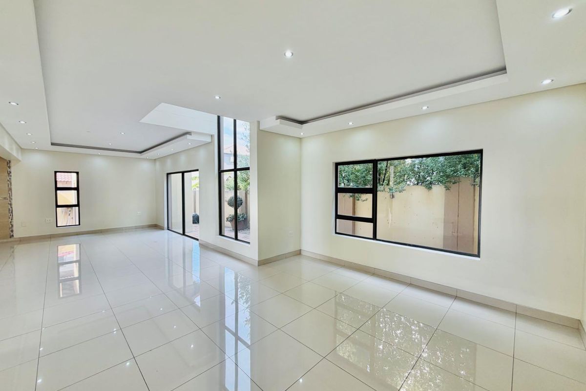 Spacious, open-plan living area featuring polished porcelain floor tiles, modern bulkhead ceilings with recessed lighting, and large aluminium-framed windows and sliding doors.