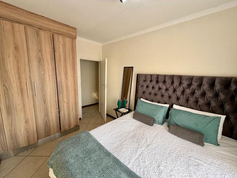 A well-maintained bedroom featuring light-toned tiled flooring, neutral walls, and a large built-in wooden wardrobe with ample storage space.