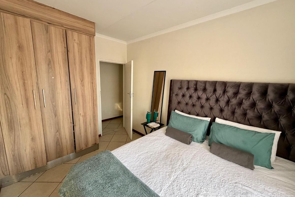A well-maintained bedroom featuring light-toned tiled flooring, neutral walls, and a large built-in wooden wardrobe with ample storage space.