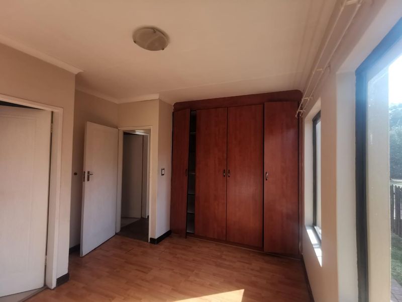 A vacant bedroom featuring built-in wooden cupboards, laminate flooring, and natural light from the side window.