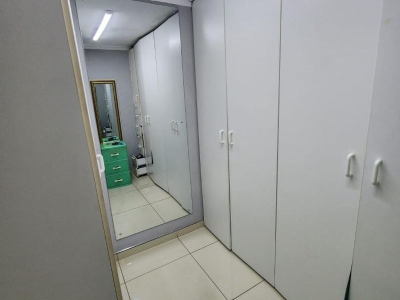 A clean hallway featuring extensive built-in white cabinetry for storage and a large full-length mirror, finished with neutral floor tiles.