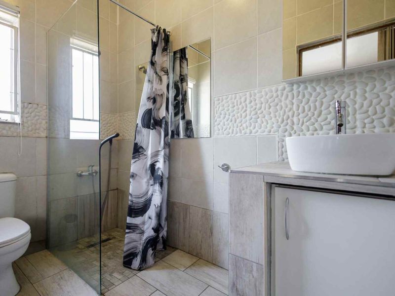 A modern bathroom featuring a glass-enclosed shower, a contemporary vessel sink on a vanity cabinet, and decorative pebble-textured wall tiling.