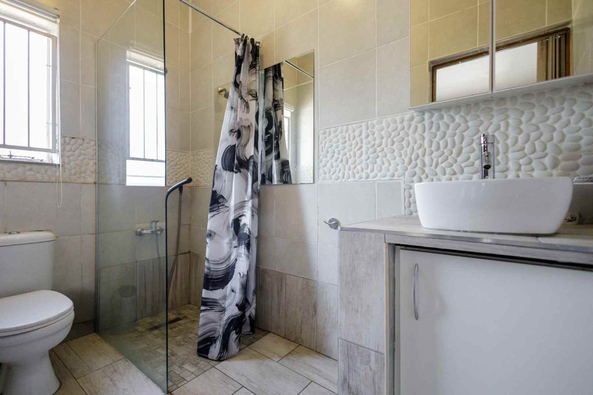A modern bathroom featuring a glass-enclosed shower, a contemporary vessel sink on a vanity cabinet, and decorative pebble-textured wall tiling.