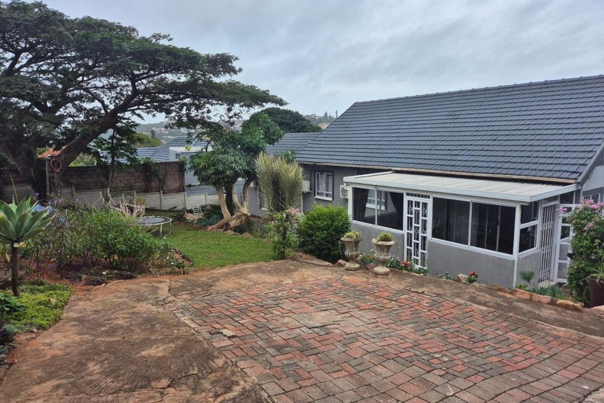Rear view of the property featuring a paved patio area, an enclosed sunroom, and a landscaped garden with mature trees.