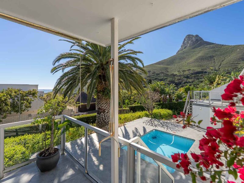 A covered balcony overlooking a private swimming pool and garden, featuring a glass balustrade and stunning mountain views.