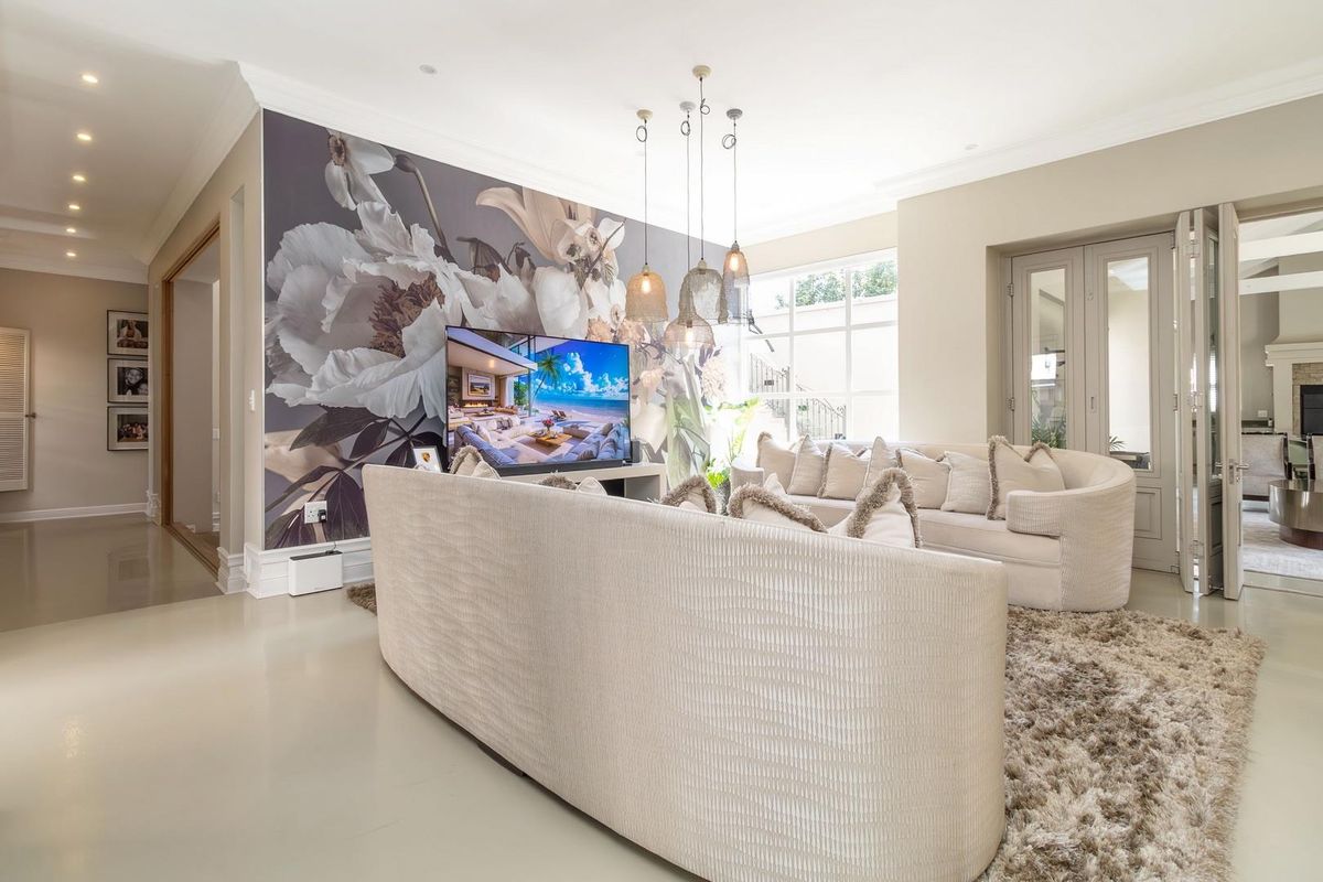 Spacious living room featuring polished flooring, recessed downlighting, decorative pendant lights, and a large feature wall with floral wallpaper.