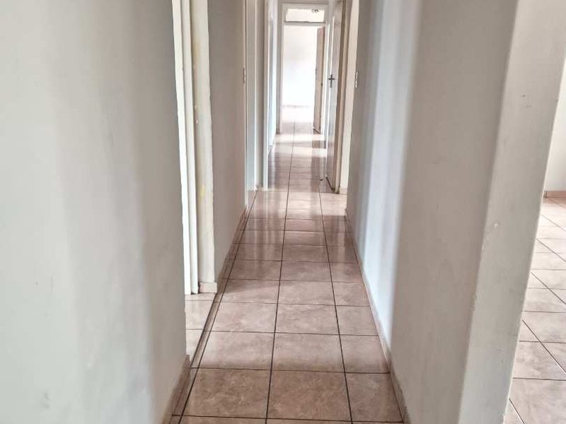 A long, empty residential hallway featuring neutral ceramic floor tiles and multiple doorways leading to adjacent rooms.