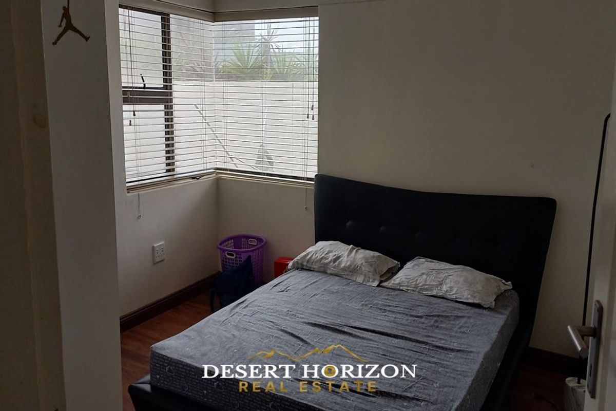 A functional bedroom featuring corner windows with fitted blinds and laminate flooring.