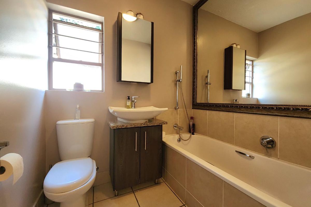 A well-maintained bathroom featuring a vessel sink on a granite vanity, a large framed mirror, a bathtub with shower mixer, and tiled finishes.