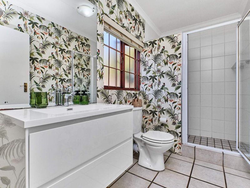 A well-maintained bathroom featuring a modern white vanity, a glass-enclosed shower, and distinctive botanical-patterned wallpaper.