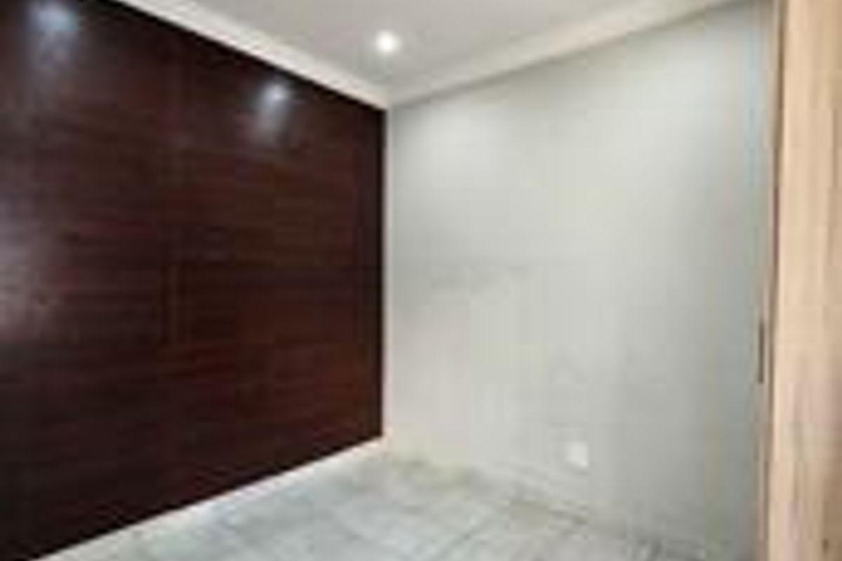 A clean, empty bedroom featuring modern tiled flooring, recessed downlighting, a built-in cupboard, and a dark wood-look feature wall.