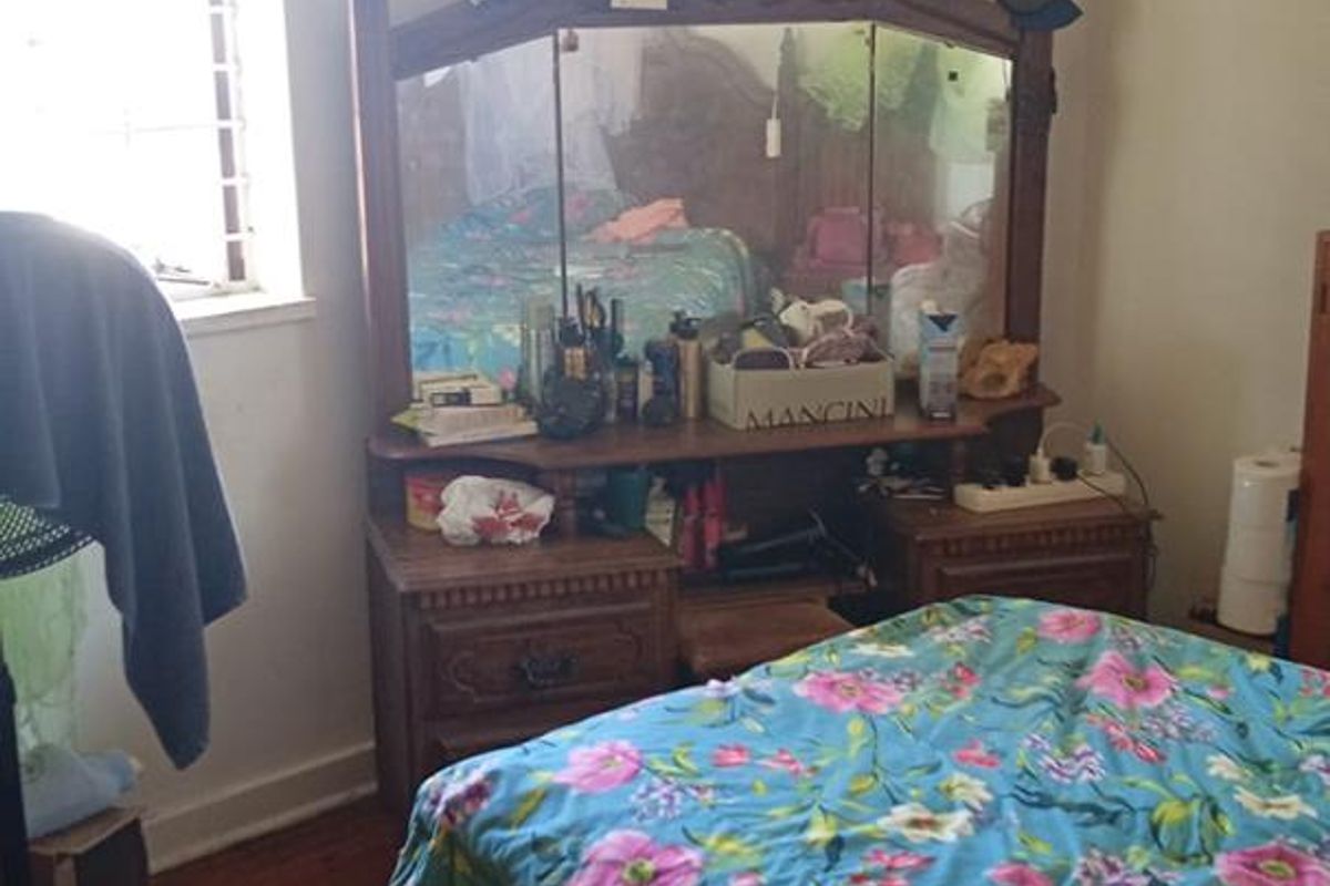 A bedroom featuring original timber flooring and a window with security bars, requiring cosmetic updates to the ceiling and floor finishes.