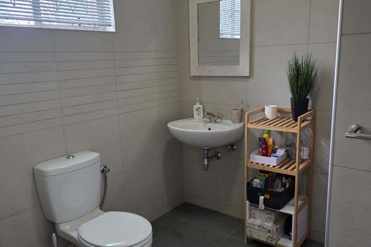 A clean and modern bathroom featuring neutral wall tiles, dark floor tiles, a wall-mounted basin, and a standard toilet.