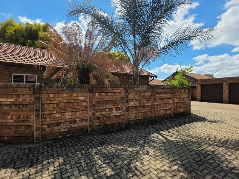 Exterior view of a townhouse complex featuring face brick boundary walls, a paved driveway, and a tiled roof structure.