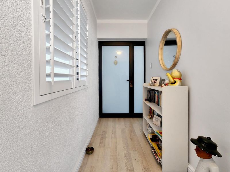 A bright entrance hallway featuring light-toned laminate flooring, a modern frosted glass front door, and white plantation shutters.