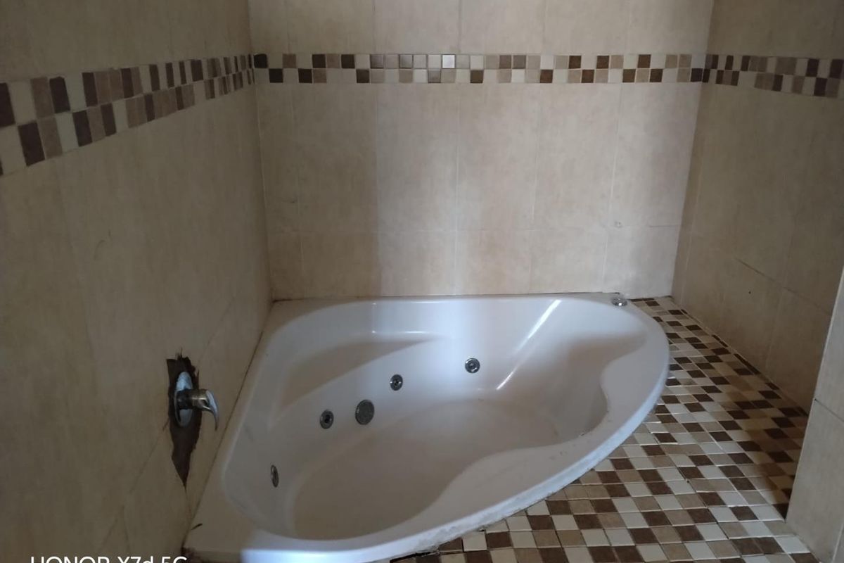 A corner bathtub in a bathroom featuring tiled walls and flooring, currently showing signs of wear and missing tile work around the faucet fixture.