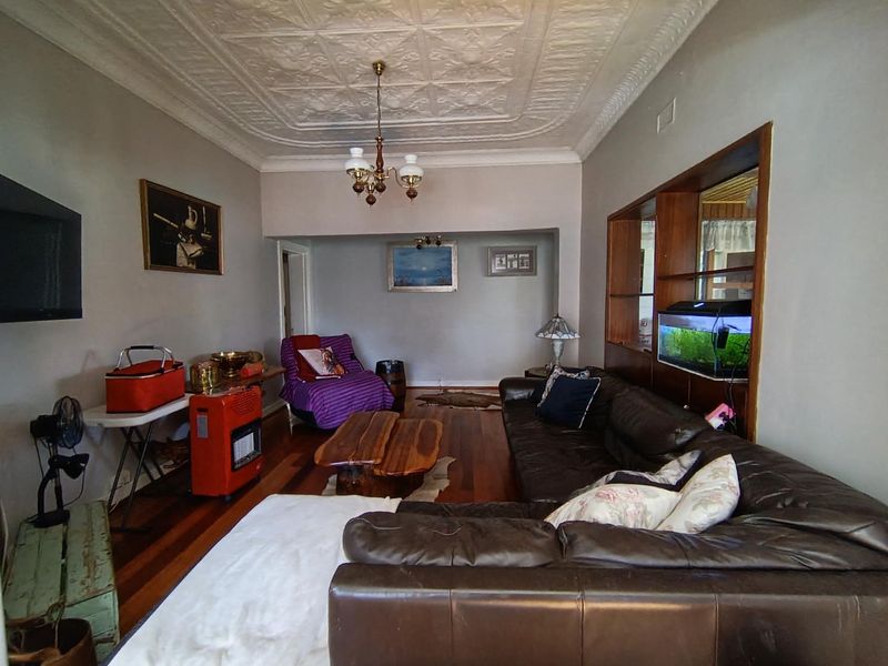 Spacious living room featuring original pressed metal ceilings, decorative ceiling rose, and polished hardwood flooring with a built-in timber display shelving unit.