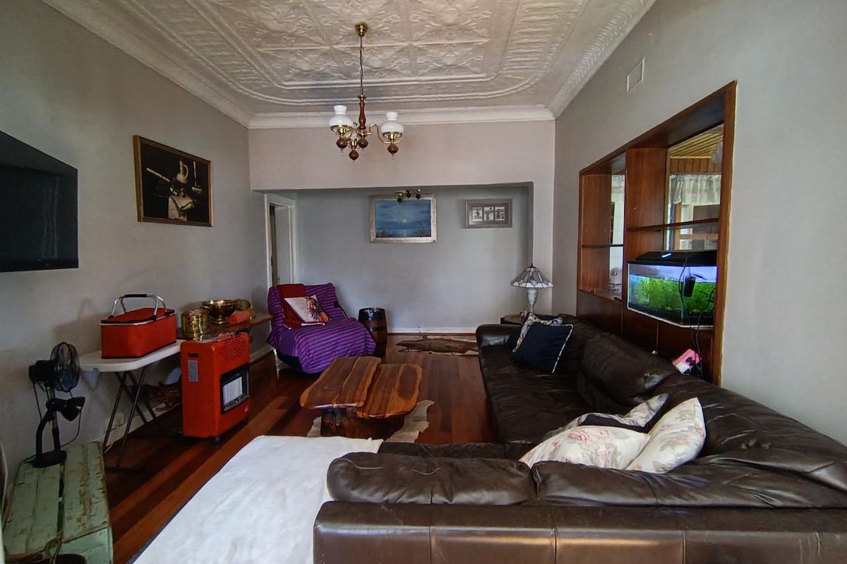 Spacious living room featuring original pressed metal ceilings, decorative ceiling rose, and polished hardwood flooring with a built-in timber display shelving unit.