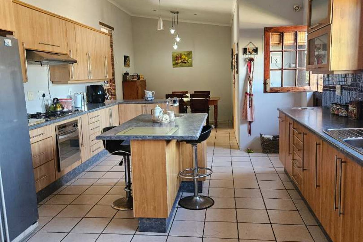 Spacious kitchen featuring light wood cabinetry, a central island with breakfast bar seating, tiled flooring, and integrated stainless steel appliances.