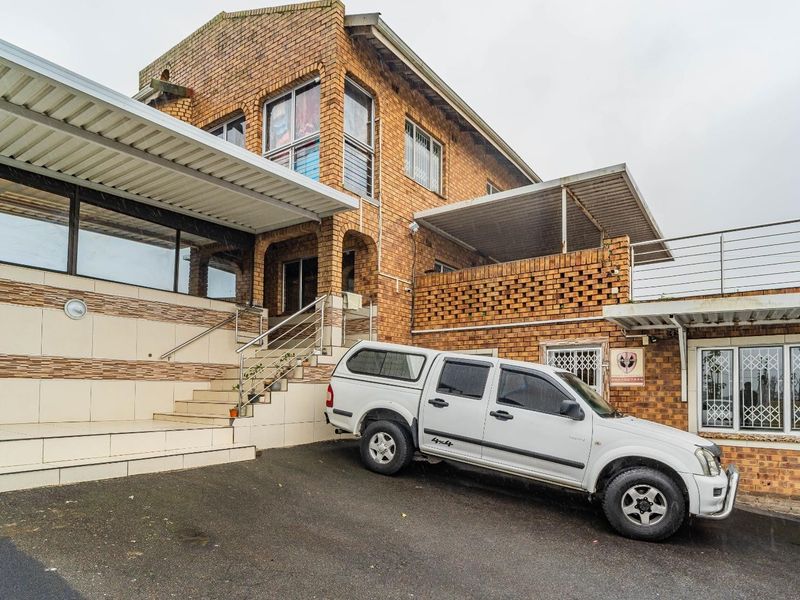 Front elevation of a multi-level brick house featuring a tiled entrance staircase, stainless steel railings, and covered patio areas.