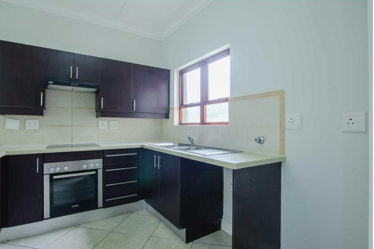 A functional kitchen featuring dark wood cabinetry, built-in oven, electric hob, extractor fan, and a double sink with tiled splashback.