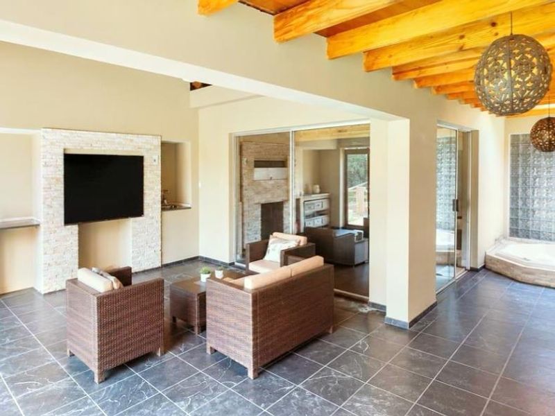 Spacious covered patio featuring exposed timber beams, a stone feature wall, tiled flooring, and a built-in spa bath area with glass block detailing.