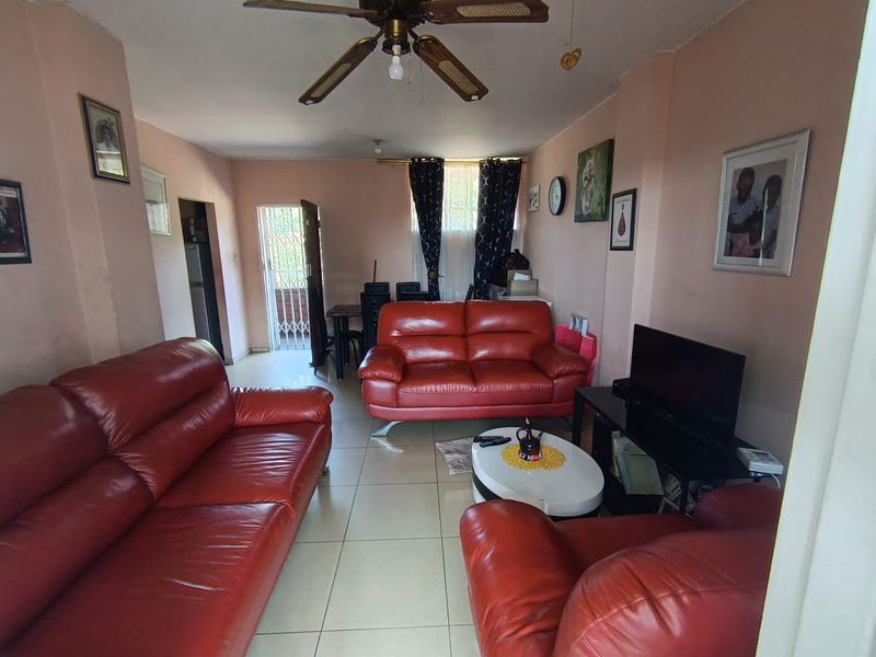 A spacious living room featuring tiled flooring, a ceiling fan, and direct access to an outdoor area through a security gate.