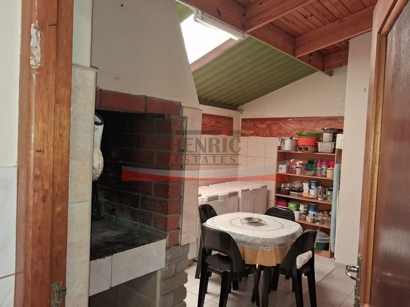 Covered patio area featuring a built-in brick braai, exposed timber rafters, and tiled flooring, offering a functional outdoor entertainment space.
