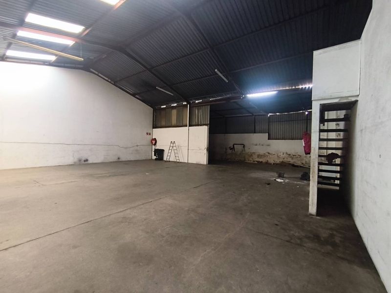 Spacious industrial warehouse unit featuring high ceilings with skylights, concrete flooring, and an internal staircase, suitable for storage or light manufacturing operations.