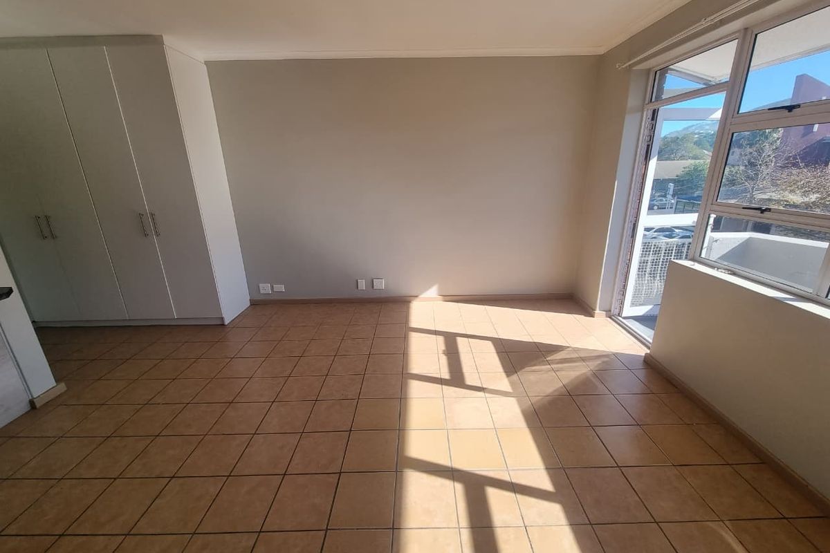 A bright, empty bedroom featuring built-in cupboards, tiled flooring, and a sliding door providing access to an outdoor area.