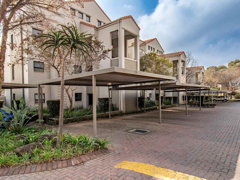 Exterior view of an apartment complex featuring covered parking carports, paved driveway, and established landscaped garden areas.